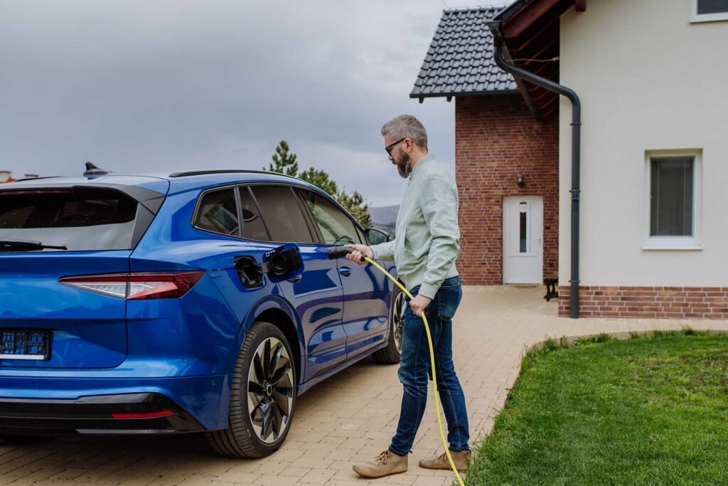 Mature man holding power supply cable and charging his electric car.